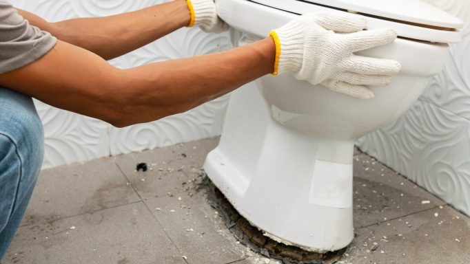 Installation d'une toilette sur sol en béton, avec des gants de protection.